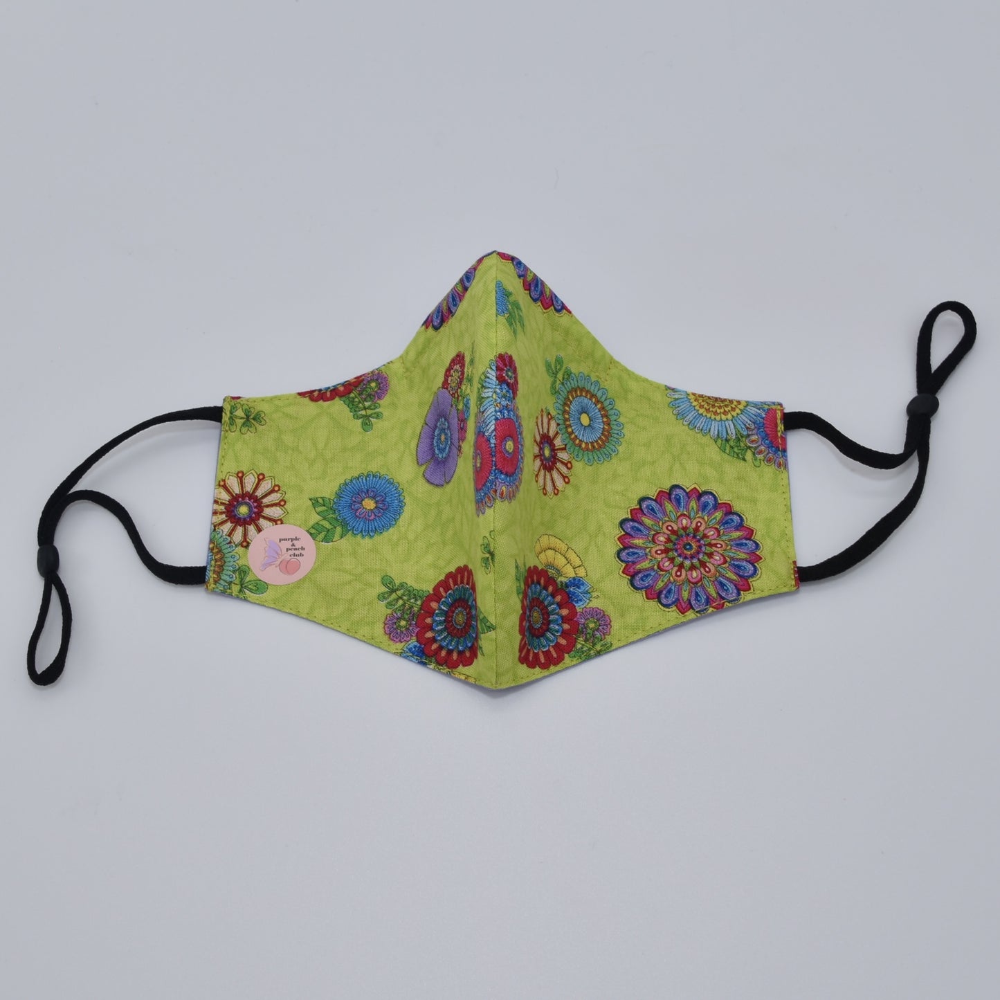 This lime green and multicolored floral print cotton face mask is reversible and double-layered, built for comfort with an adjustable nose bridge and adjustable ear straps.