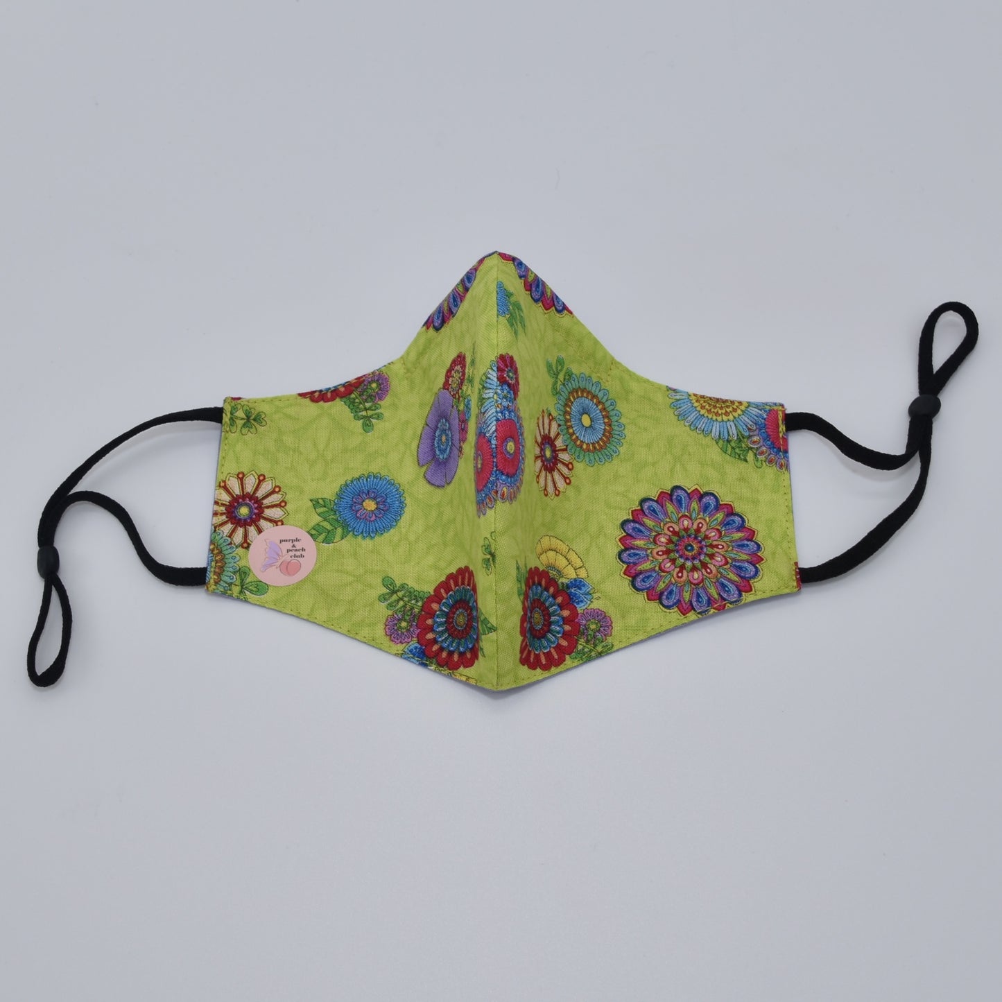 This lime green and multicolored floral print cotton face mask is reversible and double-layered, built for comfort with an adjustable nose bridge and adjustable ear straps. 